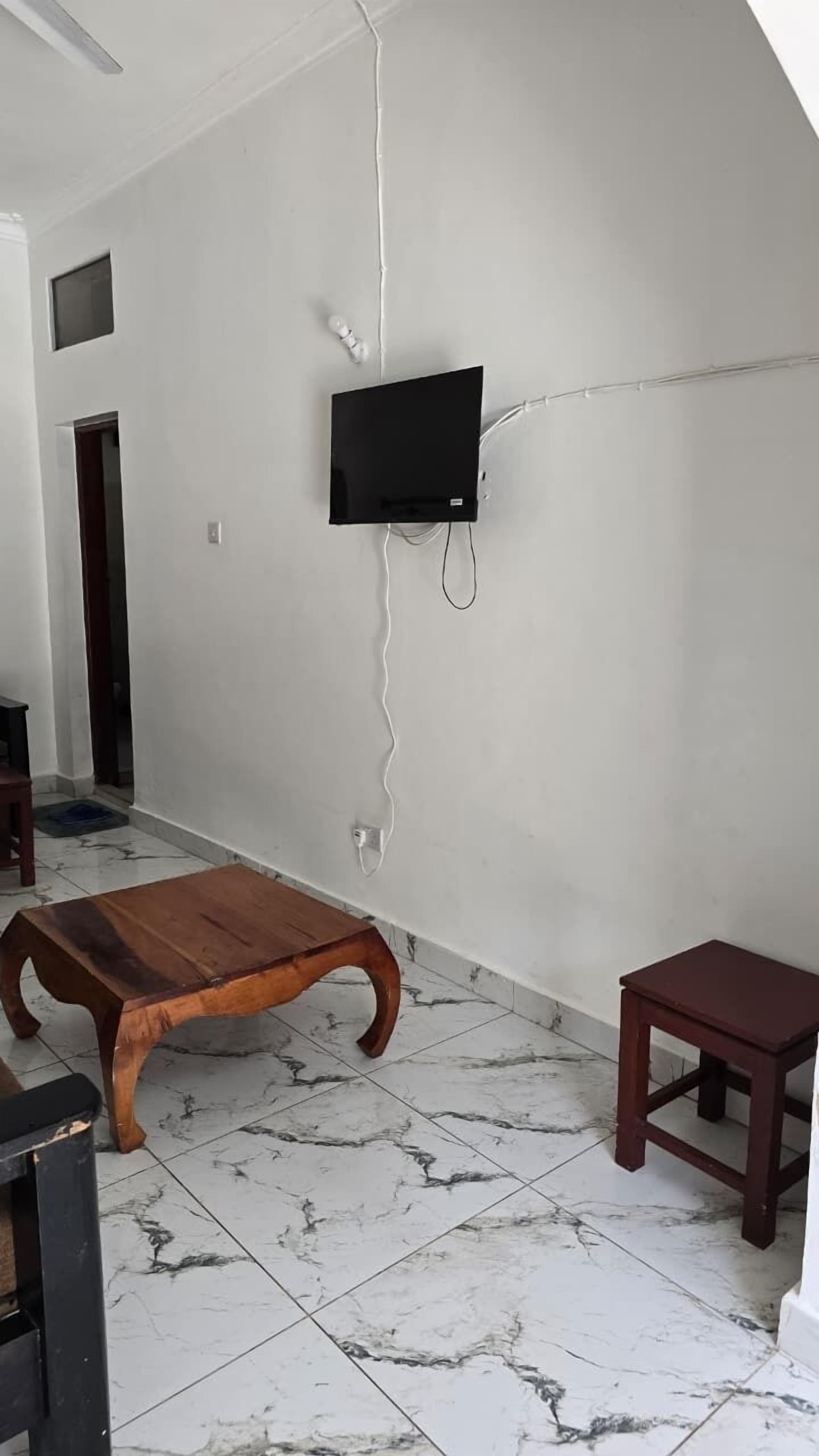 Una habitación con televisión montada en la pared, una mesa de centro de madera y un taburete pequeño de madera.