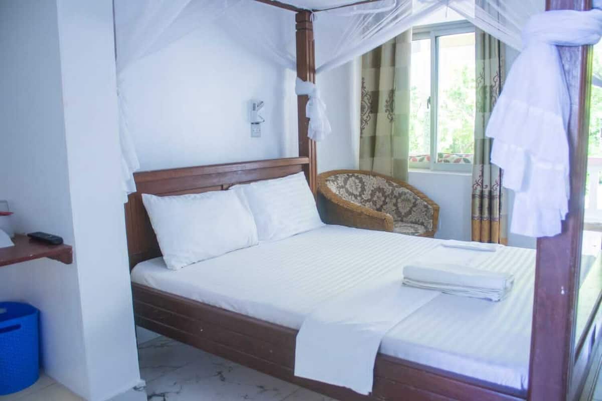 A bed with a canopy, a bedside table, a chair, and a window with curtains.