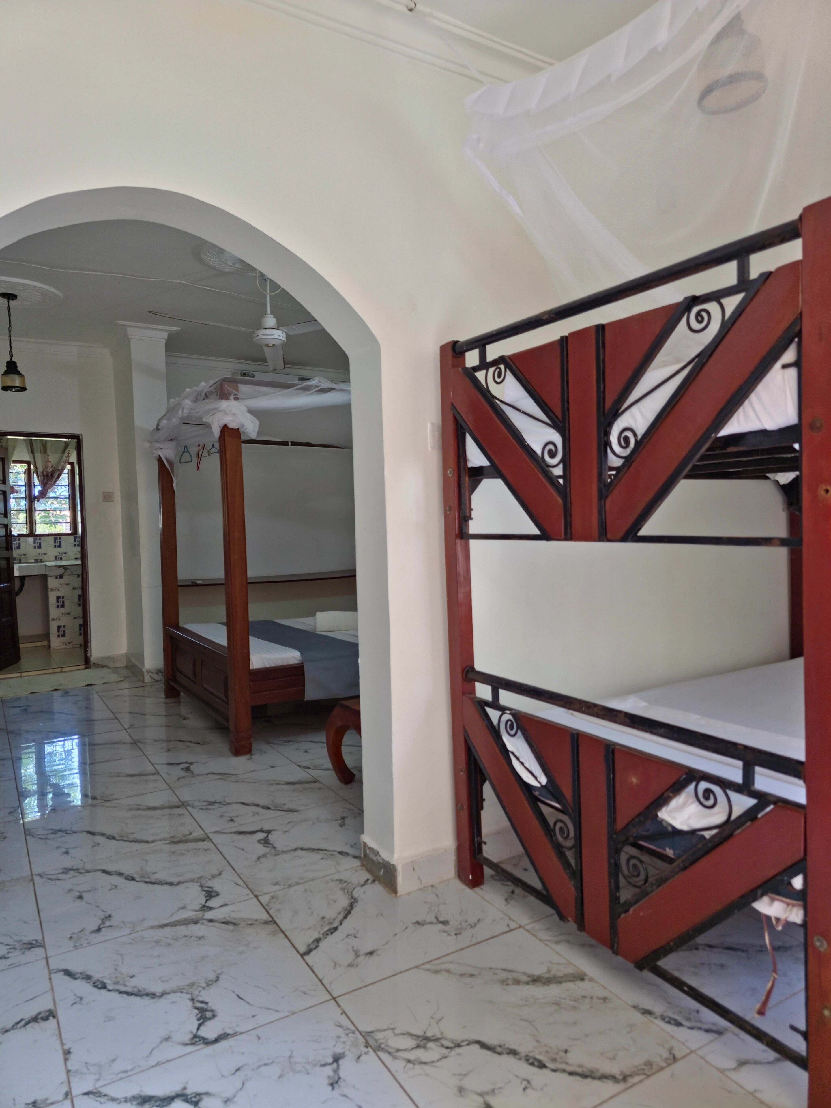 A room with a marble floor, a wooden bed with a metal frame, and a white canopy.