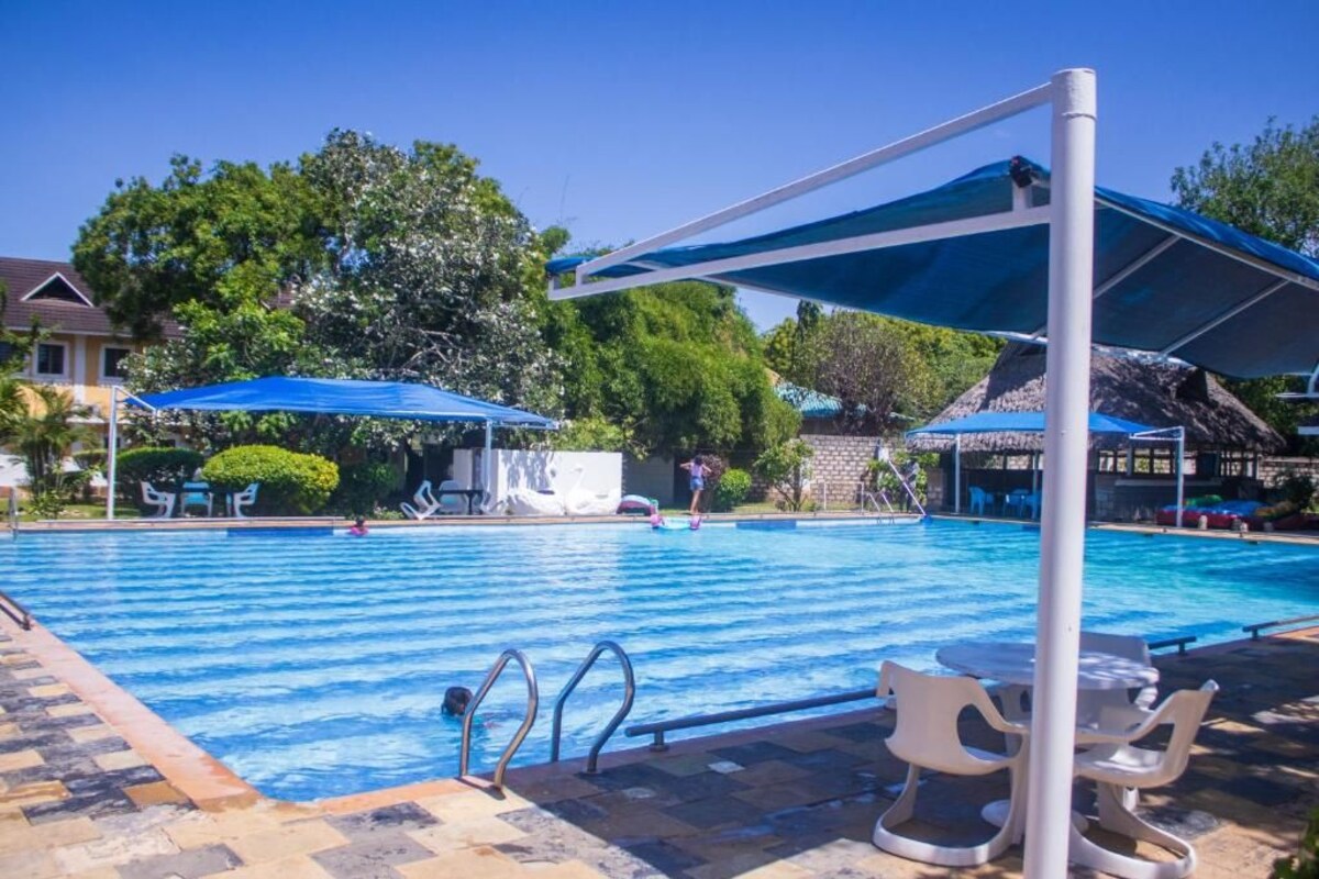 A swimming pool with blue umbrellas, lounge chairs, and a tiled deck.