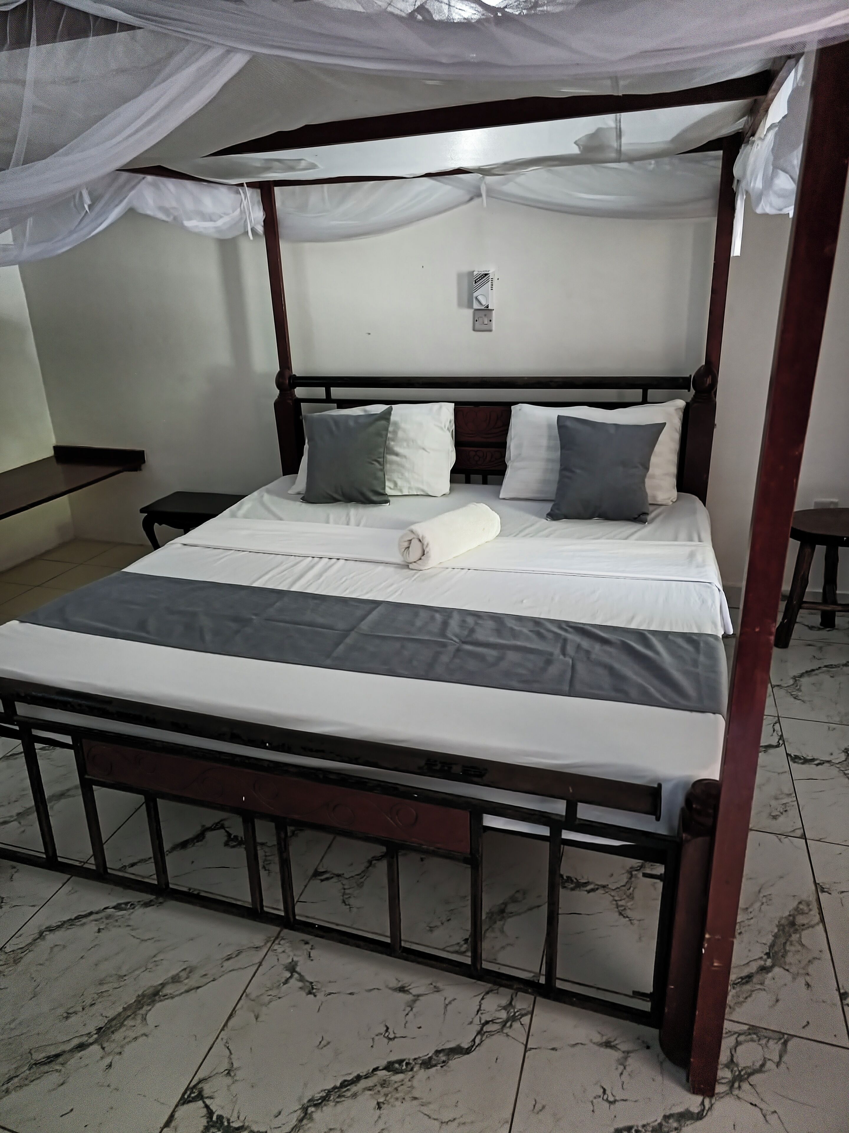 Una cama con dosel en estructura de cuatro postes, una mesita de noche pequeña y un equipo de aire acondicionado instalado en la pared.