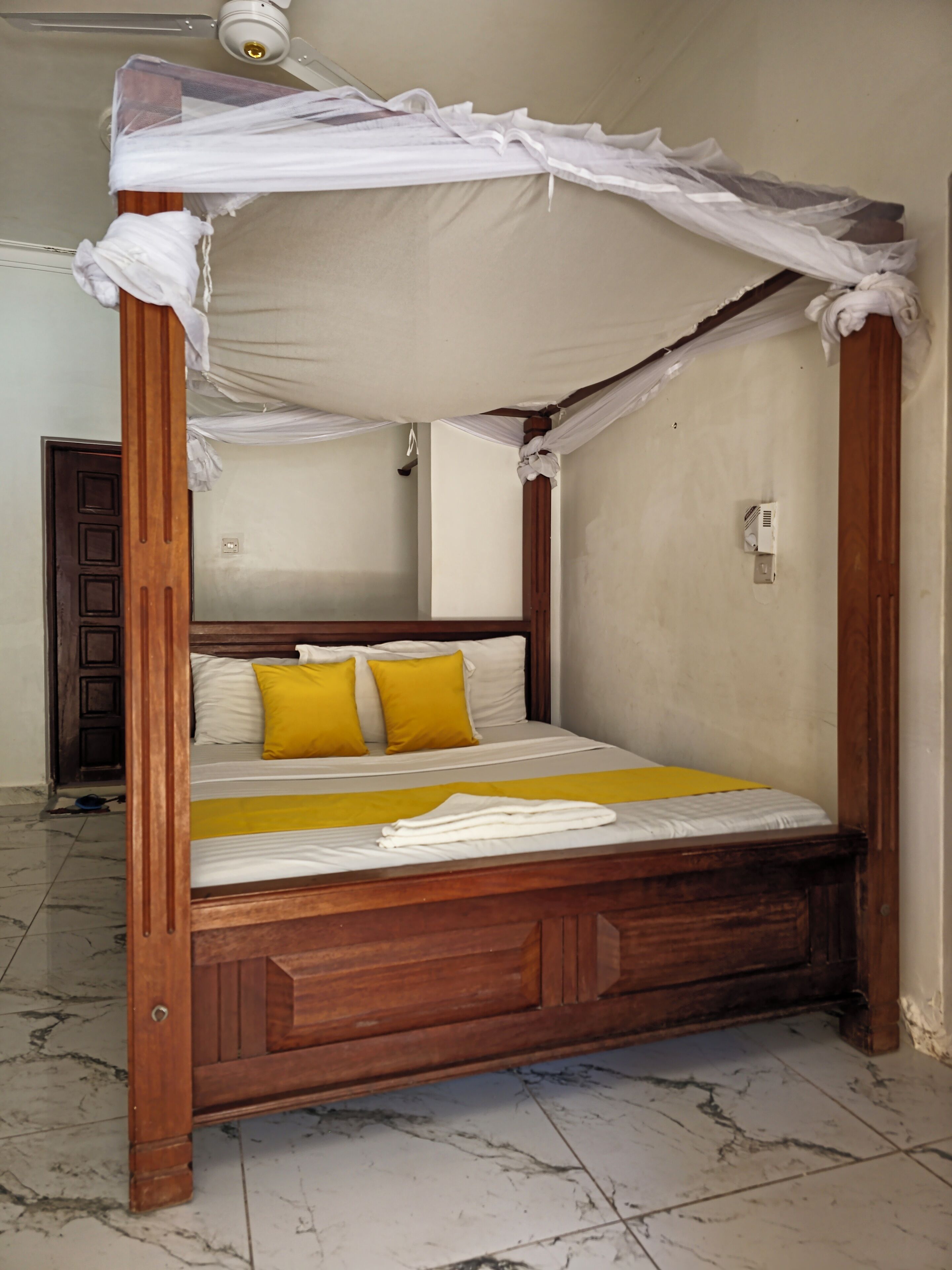 A four-poster canopy bed with wooden frame and white bedding, including two yellow pillows.