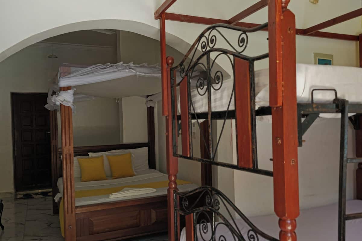 A four-poster bed with a wooden frame and metal headboard, a single bed with a wooden frame and white bedding, and a marble-tiled floor.