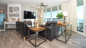 A modern living room with a black leather sofa, a wooden coffee table, and a television. There is a balcony with a view of the city. - The Palms of Destin 21117 by Compass Resorts (Destin)