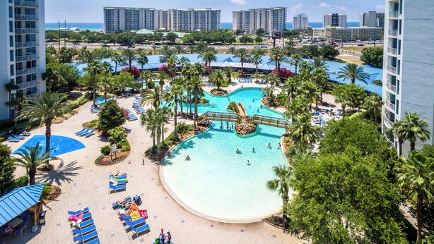 A resort with a large pool area, palm trees, and a view of the ocean. - The Palms of Destin 21117 by Compass Resorts (Destin)