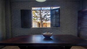 Une pièce avec une grande table en bois, une fenêtre avec des volets et une vue sur un arbre à l’extérieur.