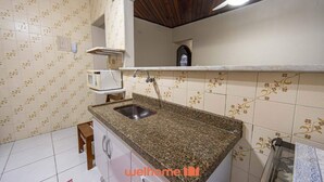A kitchen with a granite countertop, a sink, a microwave, and a ceiling fan. - Apto em Praia Grande a 500m da Praia do Caiçara (Praia Grande)