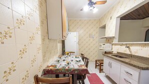 A compact kitchen with a dining table set for four, a microwave, and a refrigerator. - Apto em Praia Grande a 500m da Praia do Caiçara (Praia Grande)