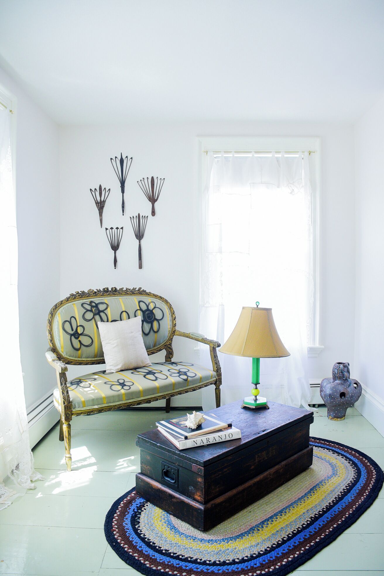 A room with a vintage sofa, a lamp, a patterned rug, and wall art.