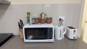 Une cuisine équipée d’un four à micro-ondes, d’un grille-pain, d’une bouilloire et de pots d’épices posés sur le plan de travail.
