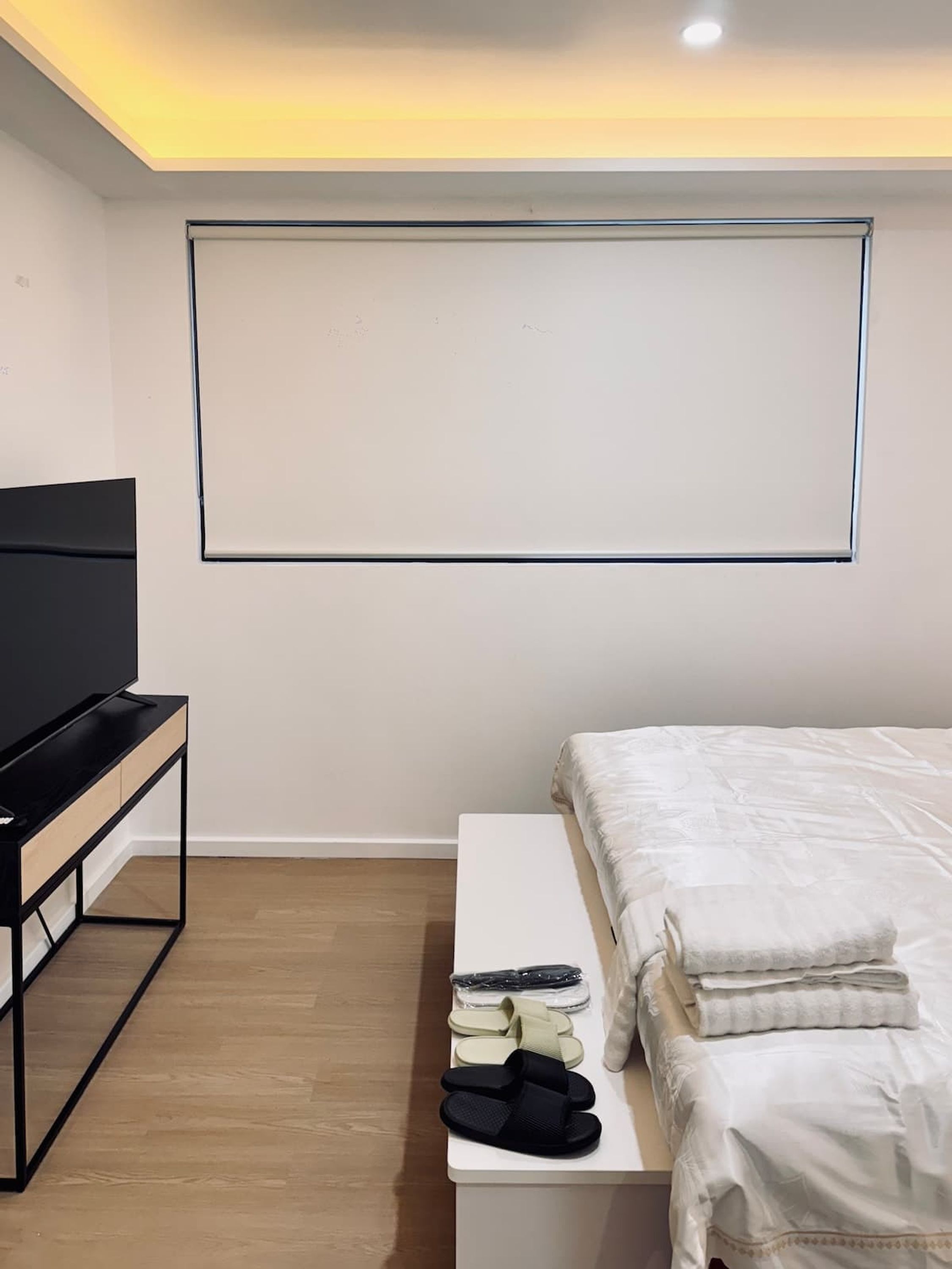 Een slaapkamer met een bed, een televisie op een standaard, een nachtkastje met slippers en een televisie aan de muur.