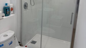 Ein modernes Badezimmer mit einer gläsernen Duschkabine, einer weißen Toilette und Ablage für Toilettenartikel.