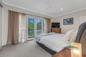 Ein Schlafzimmer mit Bett, Fernseher, einem Gemälde und einem Balkon mit Vorhängen.