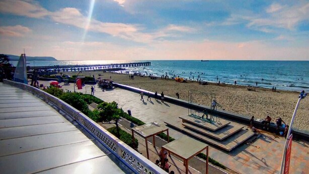 Ein Strand mit einem Steg, der sich ins Wasser erstreckt, einem sandigen Ufer und einem klaren Himmel.