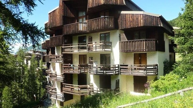 Un chalet en bois à plusieurs étages, doté de balcons et entouré de verdure.