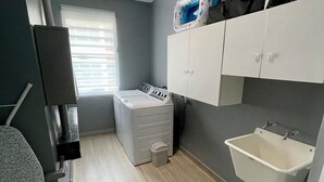 Une petite salle de bain équipée d’un lave-linge, d’un évier et d’un meuble de rangement.