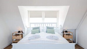 A bedroom with a white bed, two nightstands, a window with a view, and a sloped ceiling. - Studio for 2 People (Zandvoort)