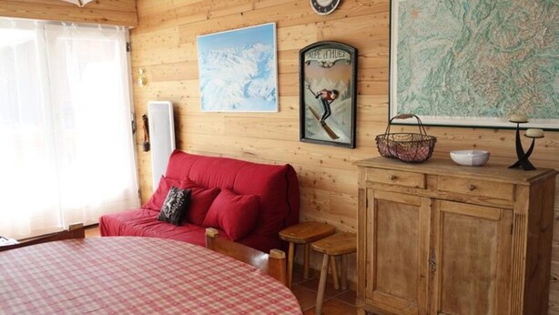 A cozy room with a red sofa, a wooden cabinet, and a bed with a checkered bedspread. - Apartment in Rif Nel Near Ski Slopes (Huez)