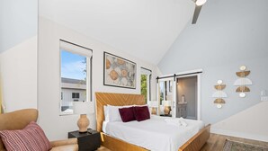 Ein modernes Schlafzimmer mit einem großen Bett, einem Holzkopfende, einem Nachttisch, einem Sessel und einem großen Fenster.
