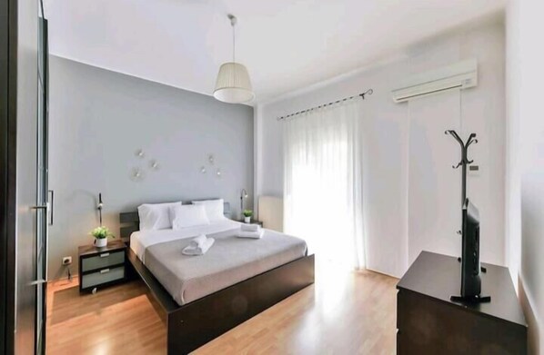A modern bedroom with a bed, bedside tables, a TV, and a coat rack. - PSV Mitropoleos  (Thessaloniki)