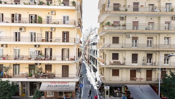A narrow street flanked by multi-story buildings with balconies, a visible storefront with a sign, and parked scooters. - PSV Mitropoleos  (Thessaloniki)