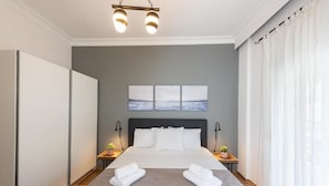 A modern hotel room with a large bed, a grey wall, a view of the sea, and a ceiling light fixture. - PSV Mitropoleos  (Thessaloniki)