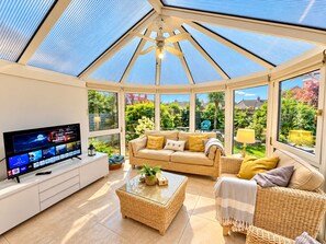 Uma sala de sol com televisão, móveis de vime e vista para o jardim.