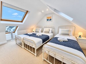 A bedroom with two beds, a skylight, and a view of a house.