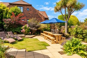 A backyard with a brick house, a wooden deck, a blue umbrella, and outdoor furniture.
