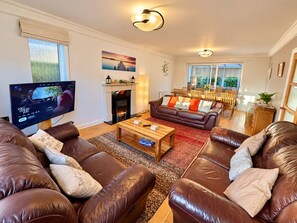 A living room with leather sofas, a fireplace, a television, and a dining area with wooden furniture. - Spacious Seaside Home in Peaceful Coastal Setting - 5 Minutes Walk to the Beach (Bournemouth)