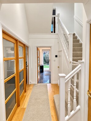 A hallway with a wooden floor, a carpeted area, and a staircase with white railings. - Spacious Seaside Home in Peaceful Coastal Setting - 5 Minutes Walk to the Beach (Bournemouth)