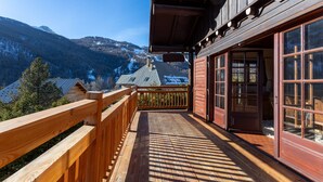 A wooden balcony with a view of mountains and a building with large windows.