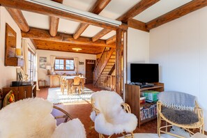 Ein rustikaler Innenraum mit freiliegenden Holzbalken, einem Essbereich, einer Treppe und einem Fernseher.