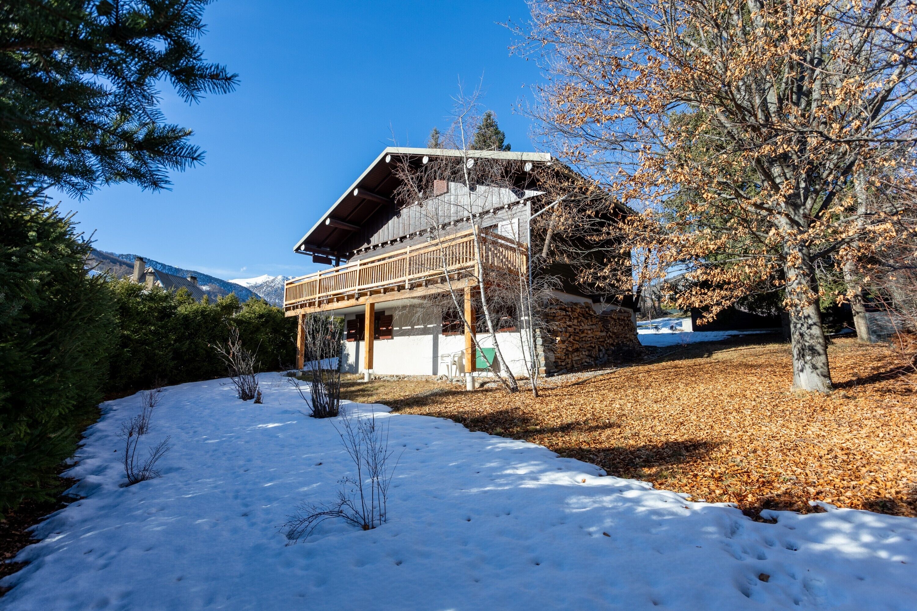 Een houten chalet met balkon, omgeven door sneeuw en bomen.