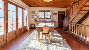 A wooden interior with a dining table, chairs, a rug, and a staircase.