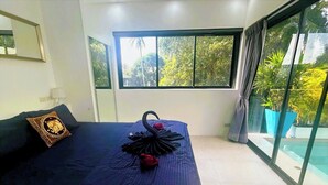 Ein modernes Schlafzimmer mit einem großen Bett, einem Zierkissen und Blick auf einen Swimmingpool durch große Fenster.