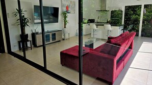 Ein modernes Wohnzimmer mit einem roten Sofa, einem Glastisch, einem Flachbildfernseher und einer Küchenzeile mit Barhocker.