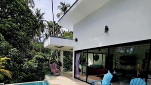 Ein moderner Poolbereich im Freien mit blauen Adirondack-Stühlen, einem überdachten Sitzbereich und üppiger tropischer Vegetation.
