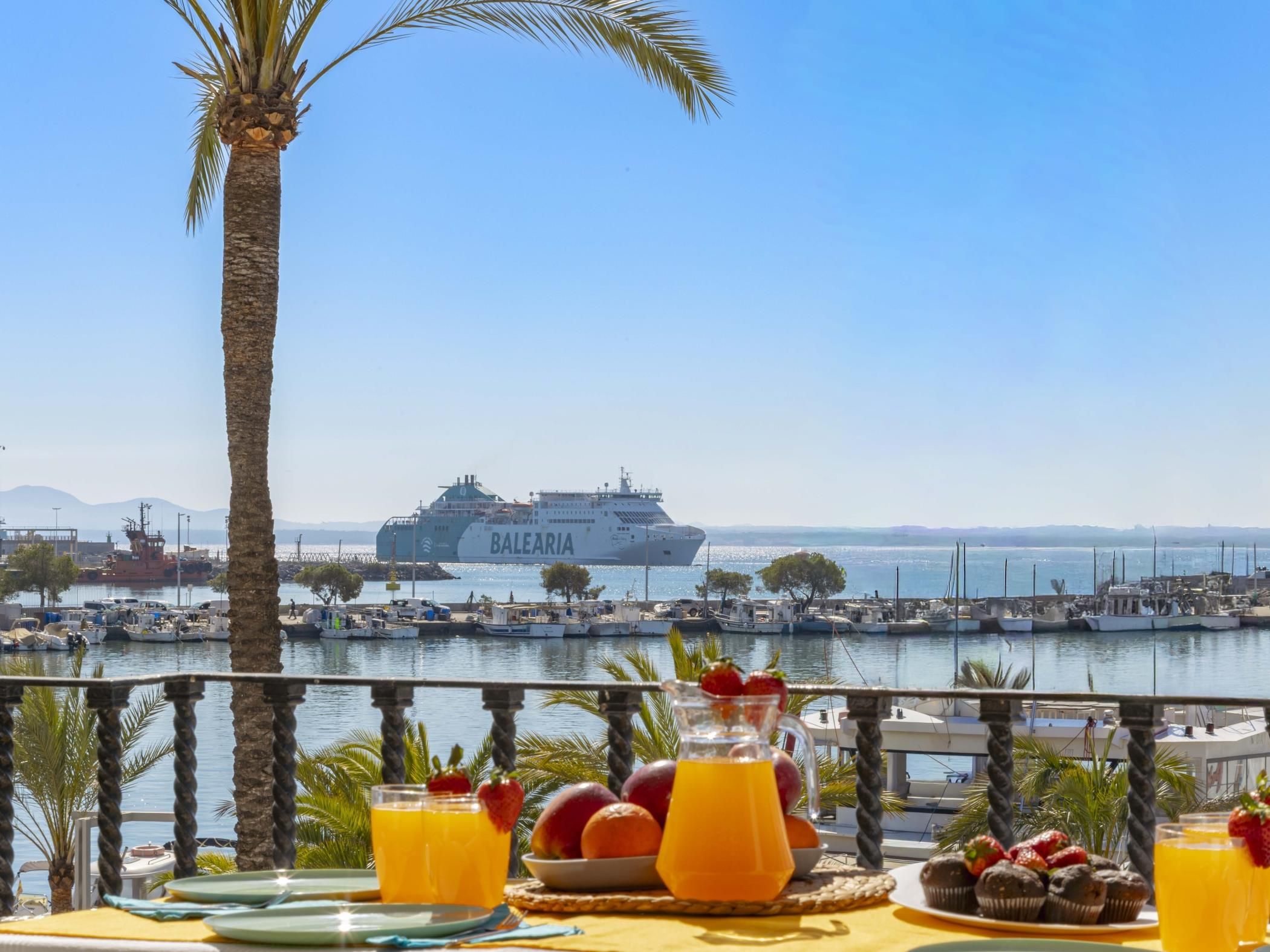 Una mesa con fruta y bebidas, un barco al fondo y una vista despejada del puerto.