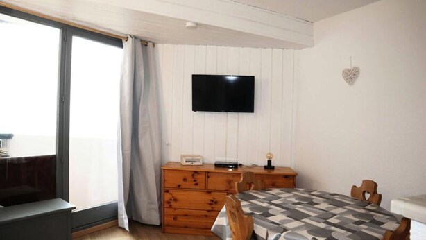 A bedroom with a bed, a dresser, a television on the wall, and a window with curtains. - Apartment in Les Orres With Ski Access (Les Orres)