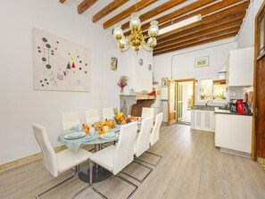 A dining area with a table set for six, a chandelier, and a kitchen visible through an open door. - Casa Can Virolla Gran ·Your house with private pool in Sa Pobla. (Sa Pobla)