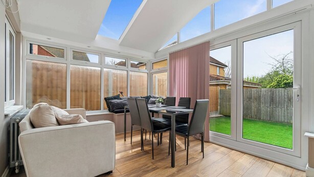 A sunlit room with a dining table, chairs, a sofa, and large windows. - 3 Bedroom Cosy-home in Hornchurch With hot tub (Hornchurch)