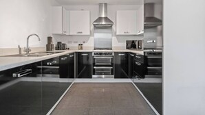 A modern kitchen with black and white cabinetry, a stainless steel range hood, and a built-in oven. - 3 Bedroom Cosy-home in Hornchurch With hot tub (Hornchurch)