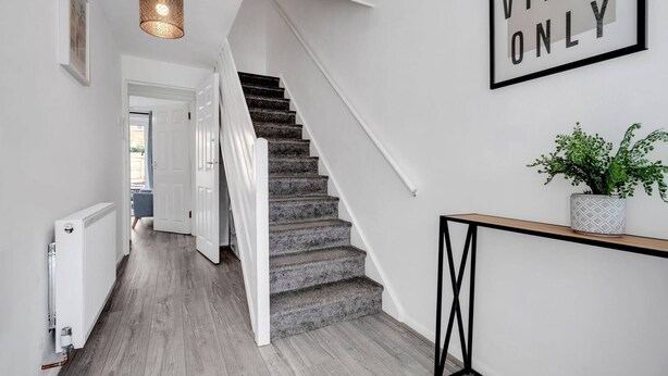 Una escalera moderna con alfombra gris y paredes blancas. Un cartel en la pared dice 'GOOD VIBES ONLY'.