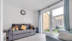 Una sala de estar moderna con un sofá gris, un reloj en la pared y un ventanal corredero que da a un patio exterior.