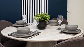 Mesa de jantar redonda com pratos cinza, copos e um vaso com planta.