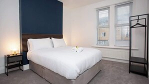 Quarto com cama, mesa de cabeceira, luminária, janela e um cabideiro.
