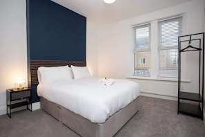 Ein Schlafzimmer mit Bett, Nachttisch, Lampe, Fenster und einer Garderobe.