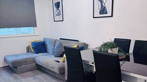 Een moderne woonkamer met een grijze bank, een eettafel met stoelen en kunstwerken in lijsten aan de muren.