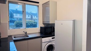 Een functionele keuken met een wasmachine, een magnetron en een koelkast.